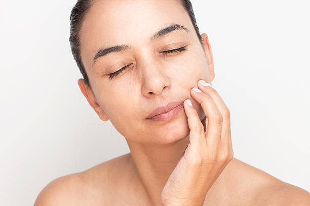 A woman with closed eyes touches her face, highlighting concerns about dull skin in a skincare context.